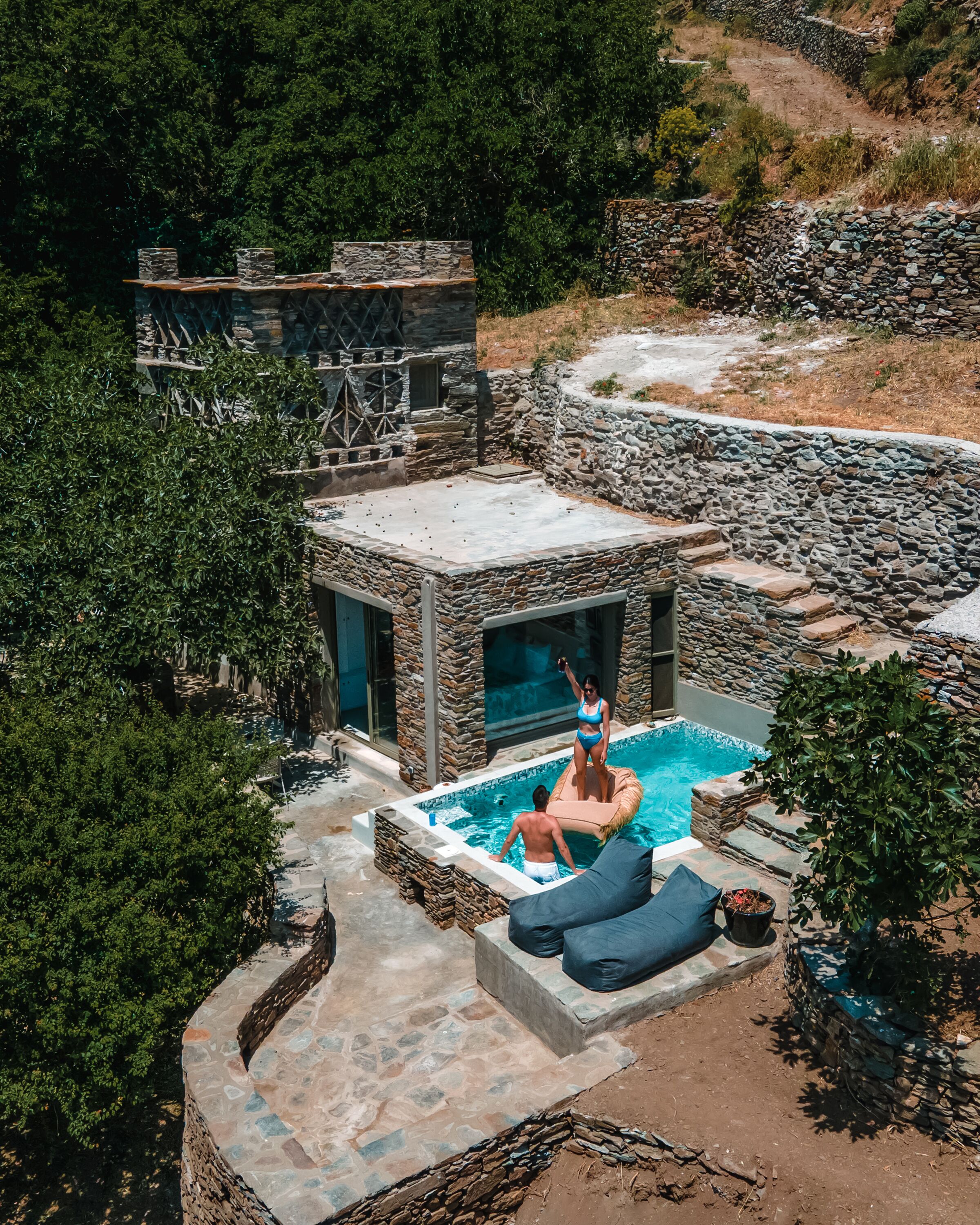 Une piscine en pierre avec un jacuzzi, entourée d’une terrasse en pierre et d’une végétation luxuriante.