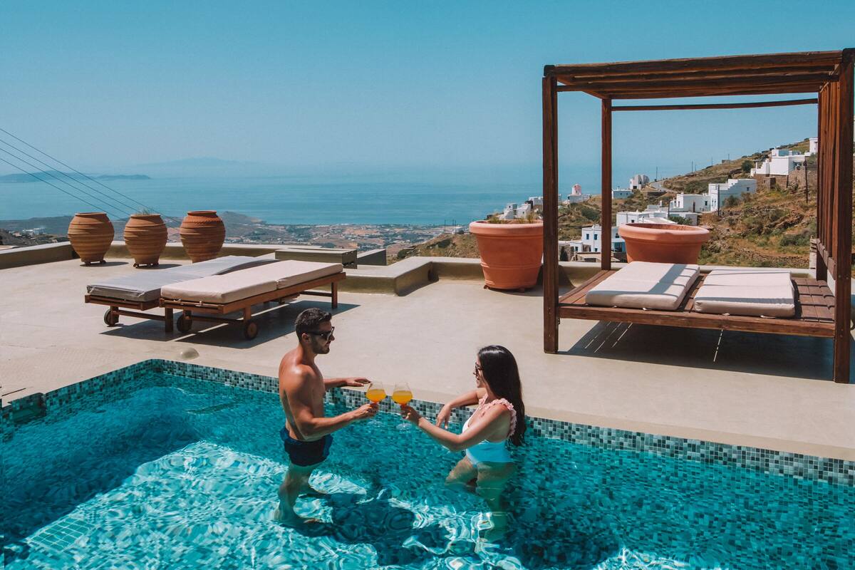 A pool area with a view of the sea, lounge chairs, and potted plants.