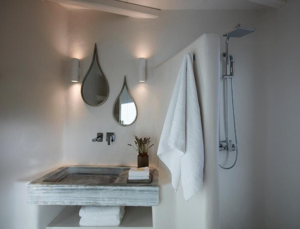 A modern bathroom with a stone sink, two wall-mounted mirrors, a towel rack, and a shower.