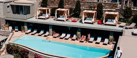 A pool area with lounge chairs and umbrellas, surrounded by stone walls and vegetation.