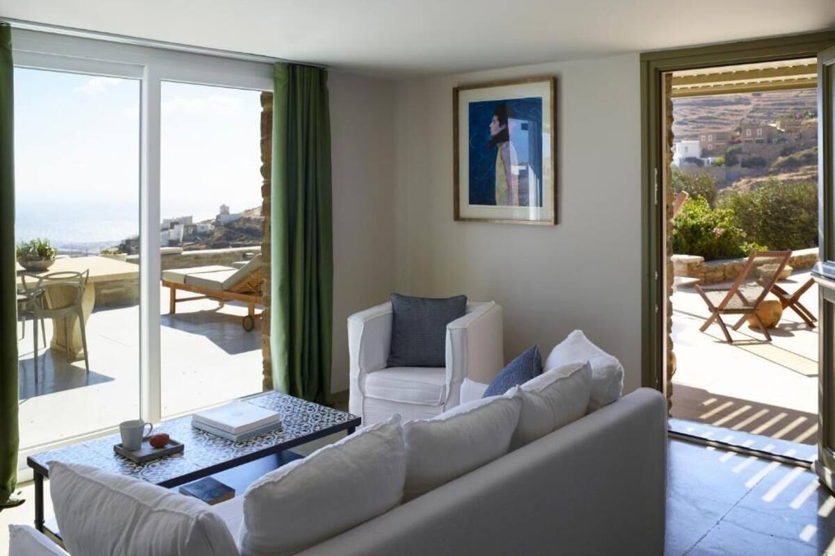 A room with a white sofa, a small table, and a chair. There is a large window with a view of a landscape.