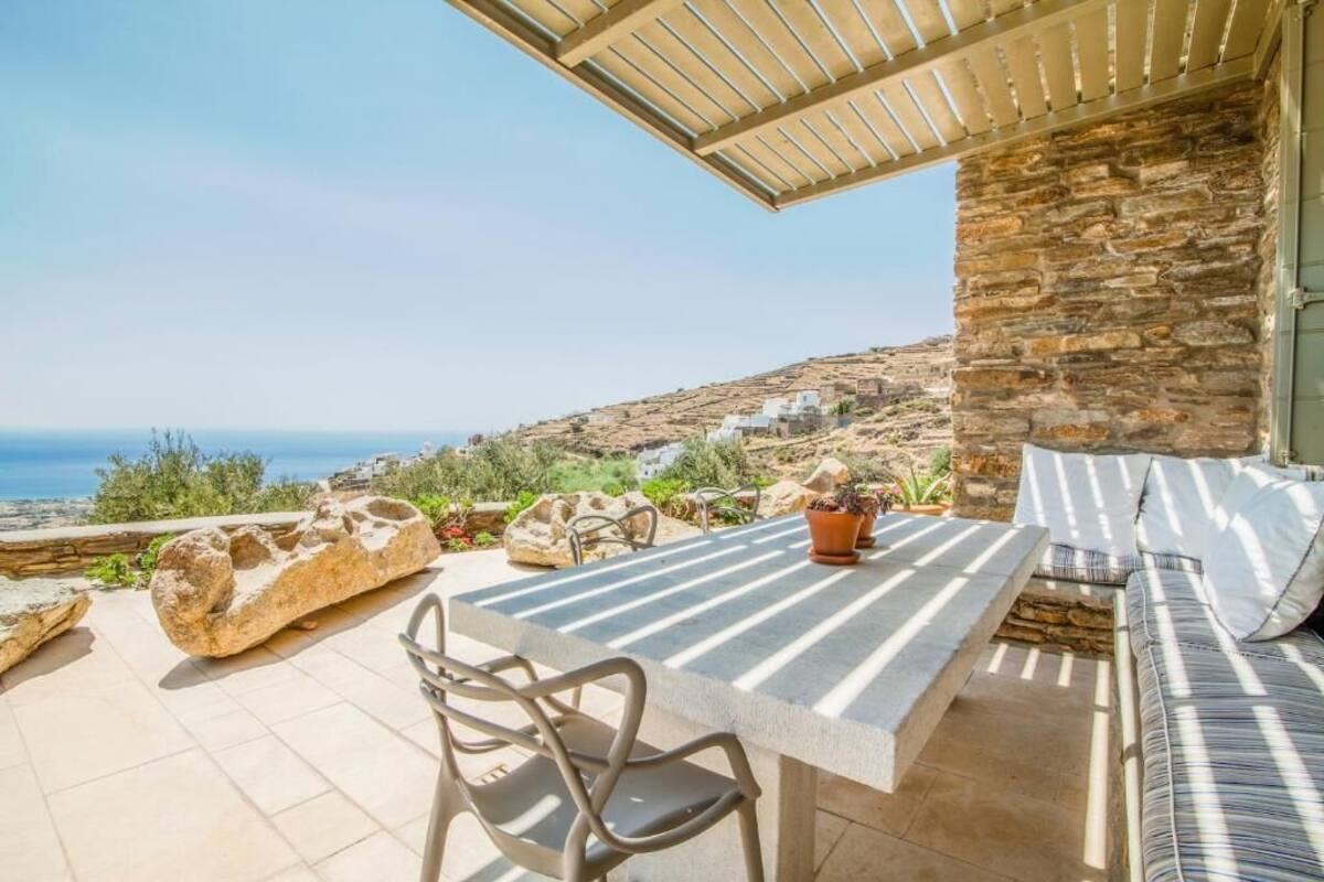 A stone house with a terrace overlooking the sea, featuring a table, chairs, and a sofa.