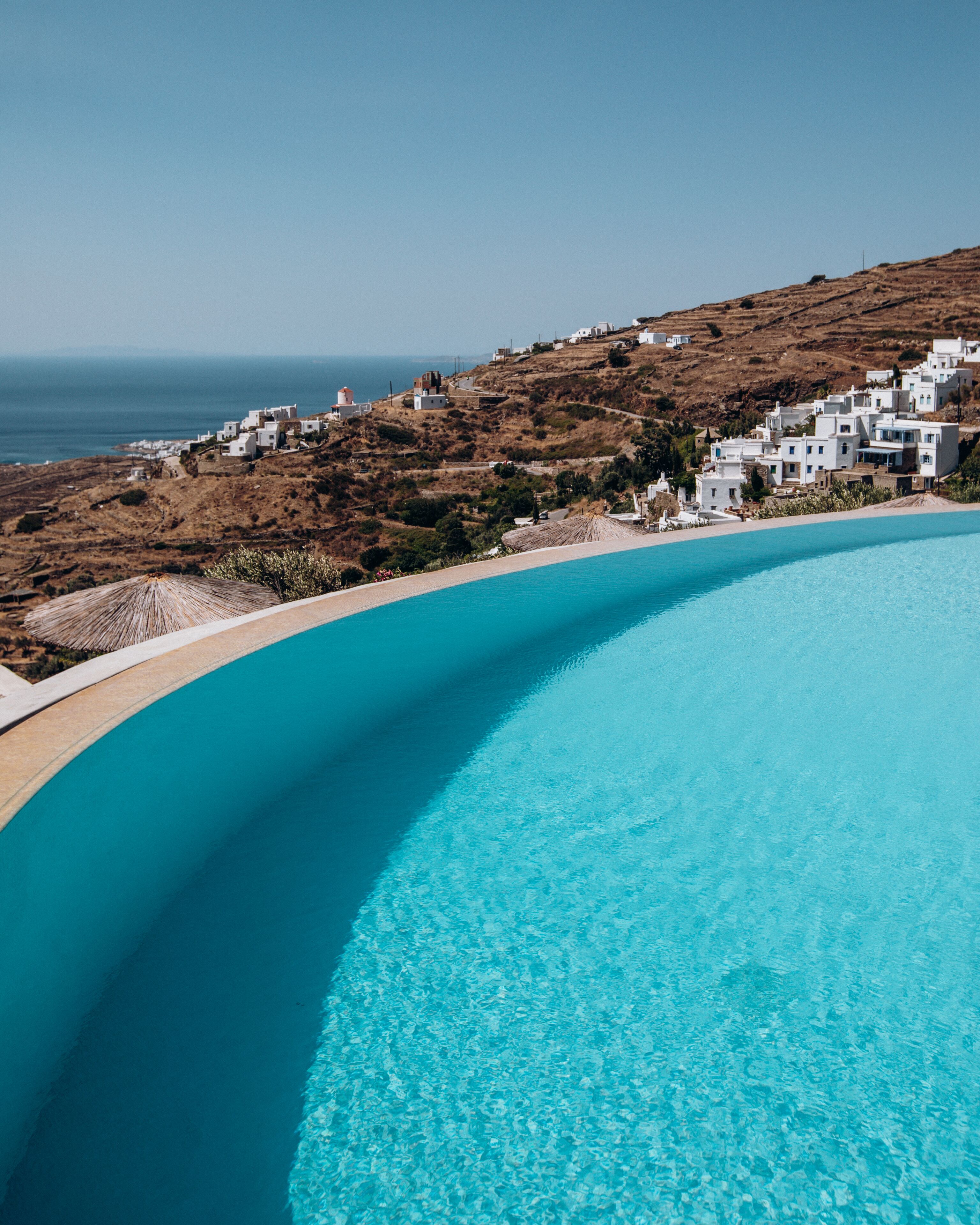 A clear blue swimming pool with a view of white buildings and a hilly landscape in the background.