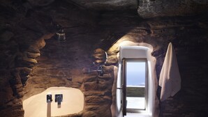 A stone-walled bathroom with a bathtub, a sink, and a window with a towel hanging on the wall. - Aeolis Tinos Suites (Tinos)