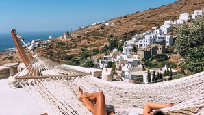 A woman relaxing in a hammock with a view of white buildings and a hillside. - Aeolis Tinos Suites (Tinos)