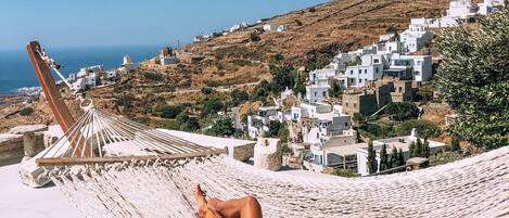 Una mujer descansando en una hamaca con vistas a edificios blancos y una colina.