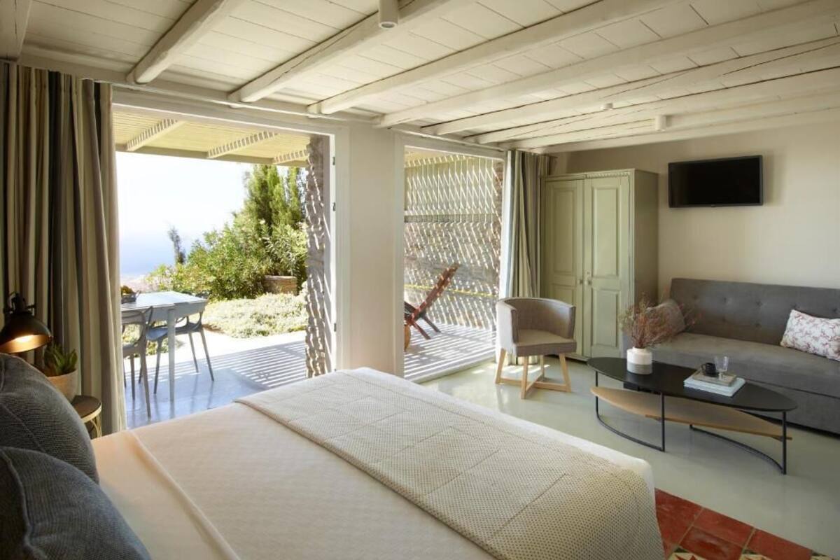 A bedroom with a bed, a sofa, a coffee table, and a TV. There is a balcony with a table and chairs.