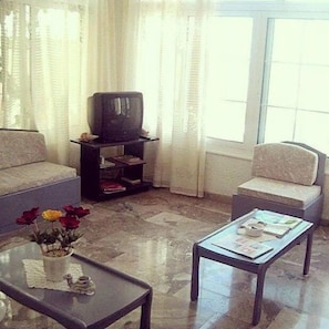 A living room with a sofa, a coffee table, a television on a stand, and a window with curtains. - Despina Hotel (Hersonissos)