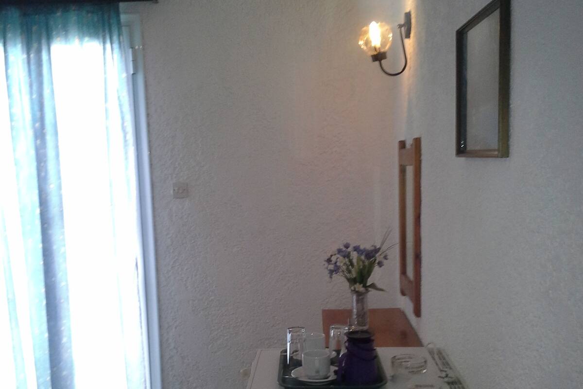 A small kitchenette with a refrigerator, a coffee maker, and a vase with flowers on a tray.