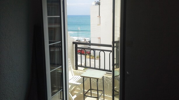A balcony with a table and chairs, overlooking a street and the ocean. - Despina Hotel (Hersonissos)