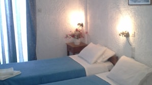 A hotel room with two beds, a nightstand with a vase of flowers, and a wall-mounted lamp. - Despina Hotel (Hersonissos)