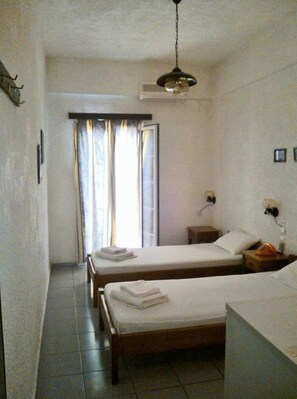 A hotel room with two beds, a bedside table with a lamp, a window with curtains, and a wall-mounted telephone. - Despina Hotel (Hersonissos)