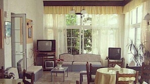 A living room with a sofa, TV, dining table, chairs, and a window with curtains. - Despina Hotel (Hersonissos)
