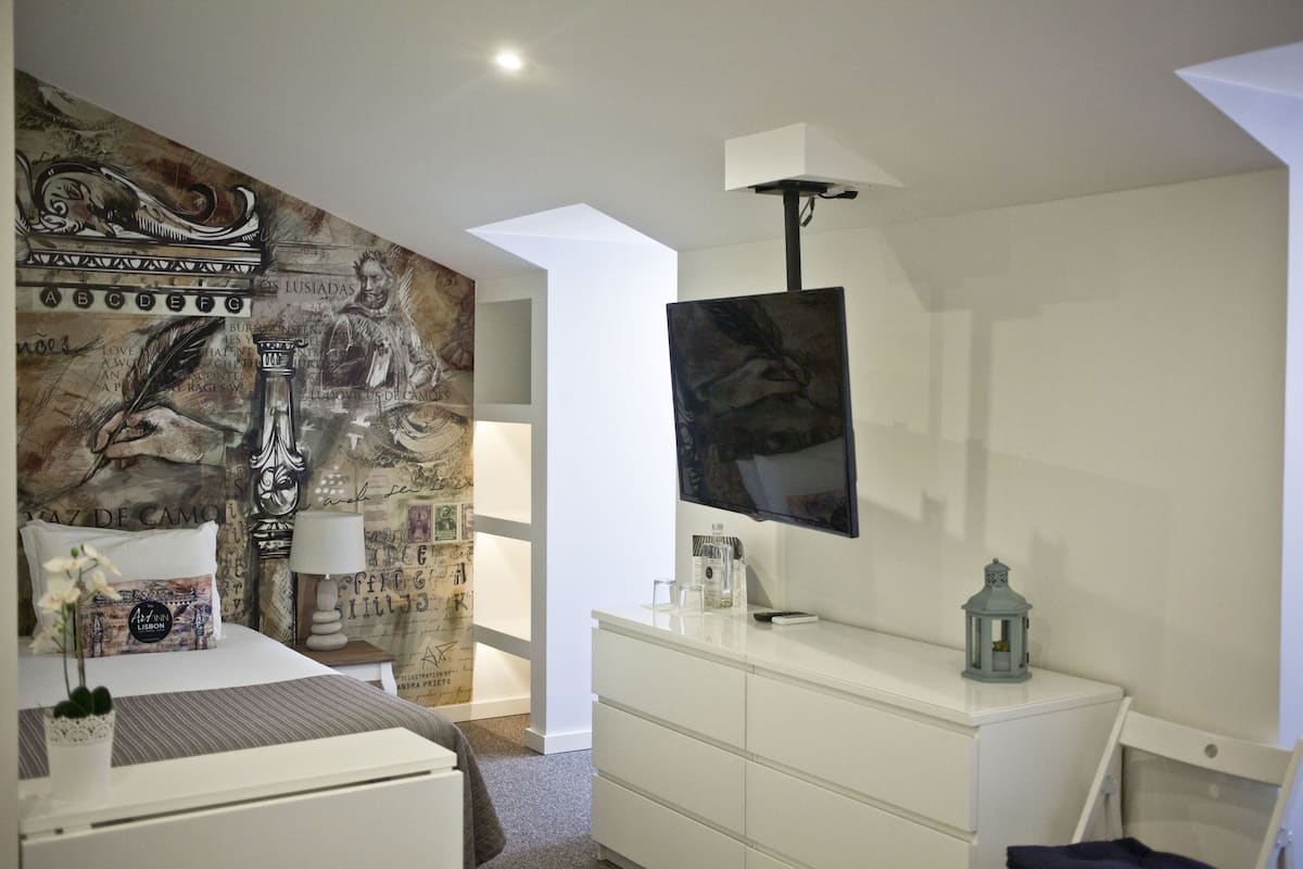 Quarto moderno com cama, cômoda, televisão e um detalhe decorativo na parede.