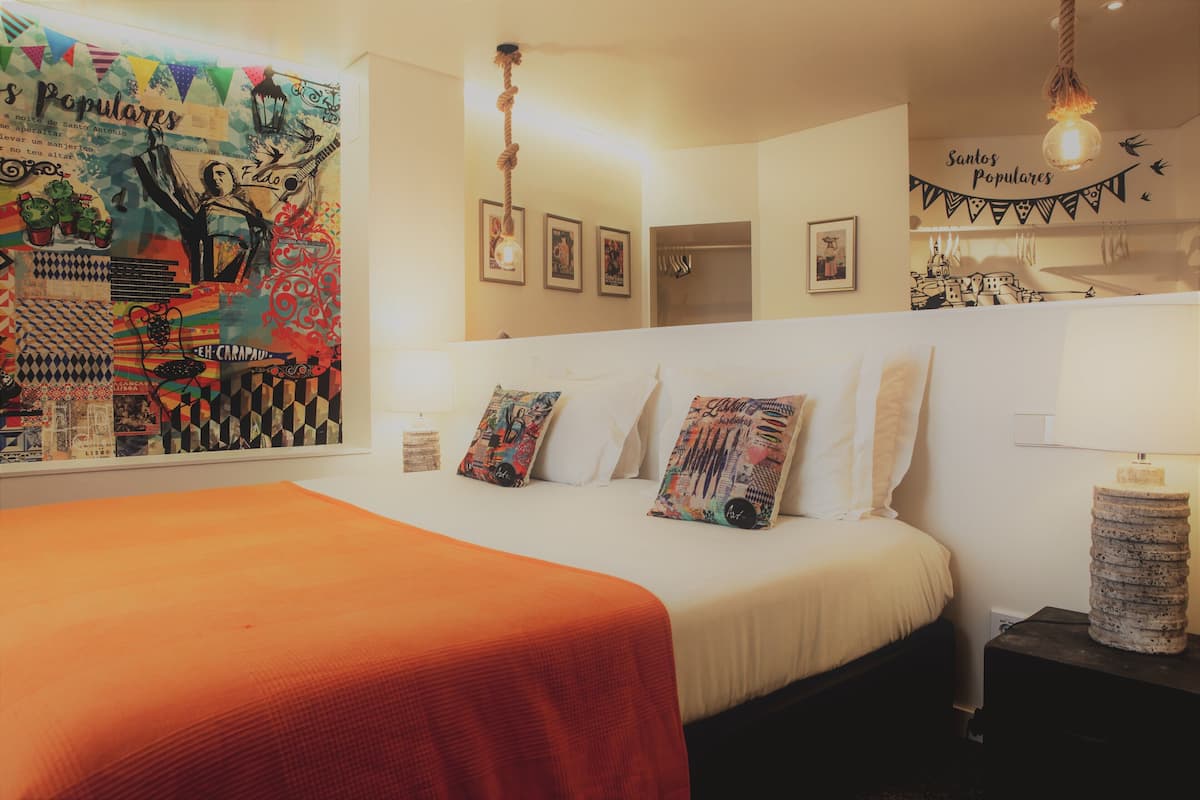 Quarto com cama, almofadas, mesa de cabeceira, parede com obra de arte e luminária pendente.