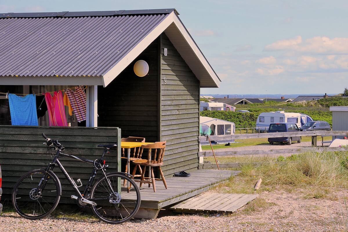 A small wooden cabin with a porch, a bicycle, and a table with chairs.