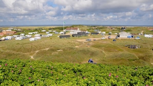 Un terrain de camping aménagé avec des emplacements pour camping-cars, des tentes et des chalets, entouré de prairies verdoyantes et offrant une vue lointaine sur la mer.