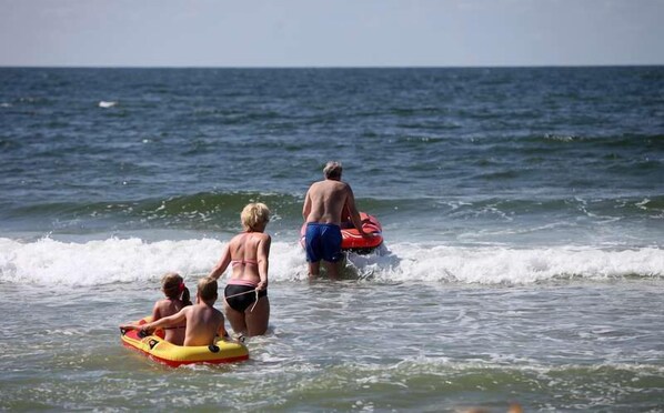 A beach scene with people in the water, some on inflatable rafts.