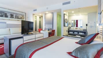 Ein modernes Hotelzimmer mit einem Bett, einem Schreibtisch, einem Fernseher, einem Spiegel und einem Badezimmer.