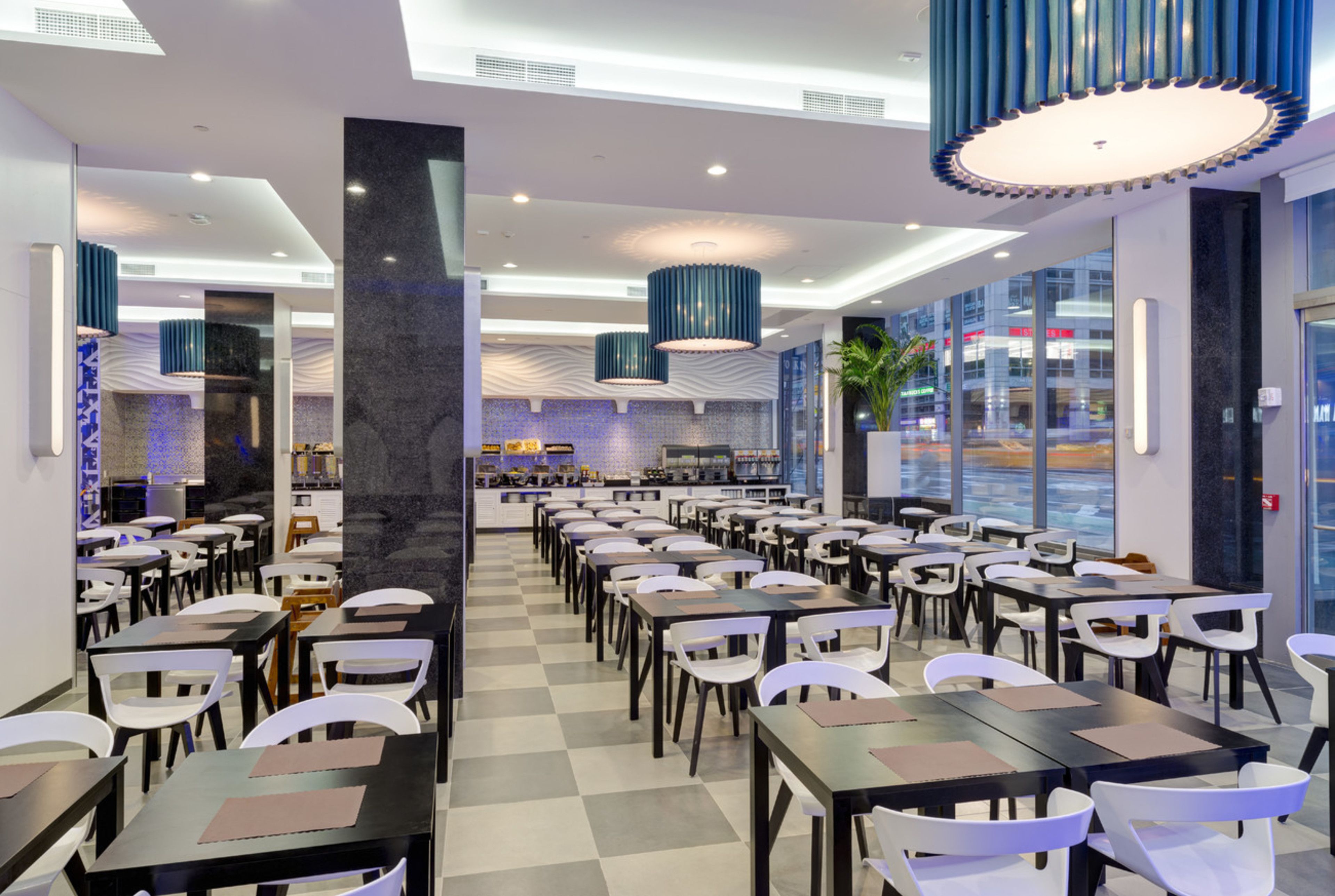 A modern restaurant with a checkered floor, multiple tables and chairs, and blue pendant lights.