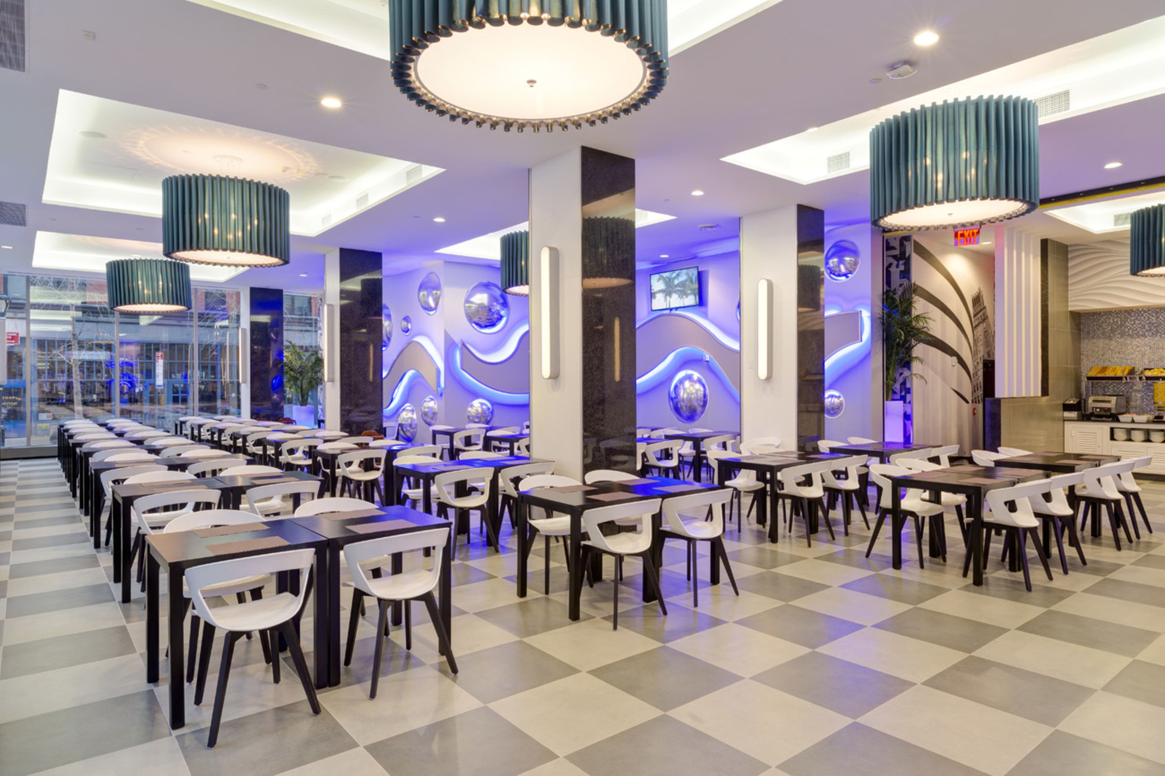 Un comedor amplio con varias mesas y sillas, luminarias modernas y piso a cuadros.