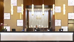 A hotel reception desk with a modern design, featuring a large chandelier, multiple screens displaying floral patterns, and a reception area with a wooden backdrop.