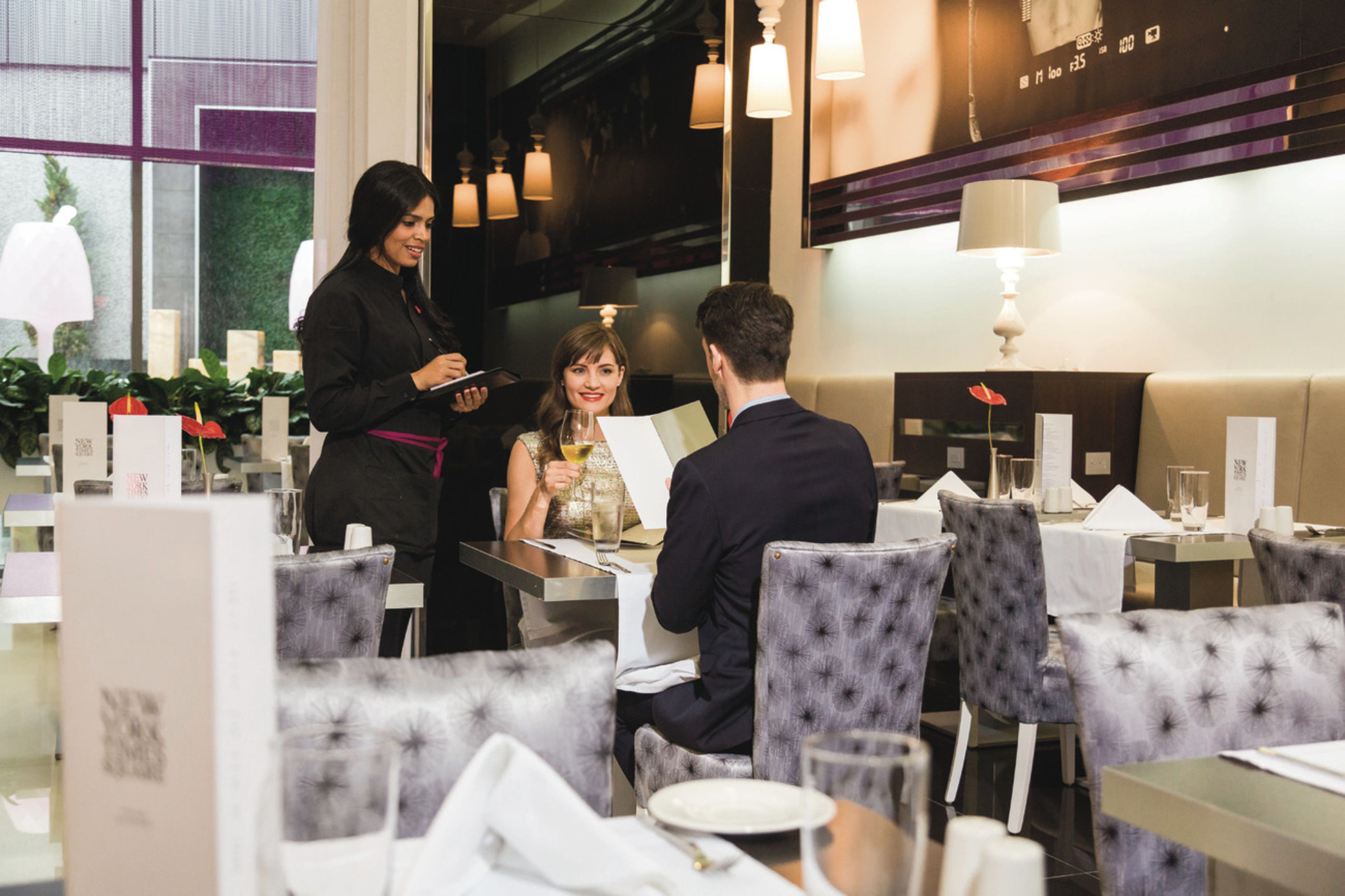 L’intérieur d’un restaurant, où l’on voit un serveur s’occuper d’un couple assis à une table.