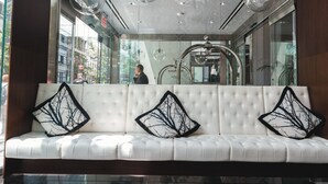 A white tufted sofa with black tree-patterned cushions in a modern lobby with glass walls and hanging spherical light fixtures.