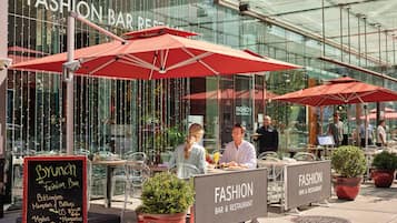 An outdoor dining area with red umbrellas, a sign for 'Fashion Bar & Restaurant', and a menu board listing brunch items.