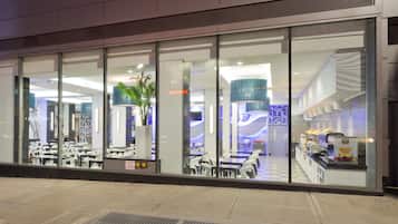 A modern restaurant with a glass facade, interior seating, and a visible kitchen area.