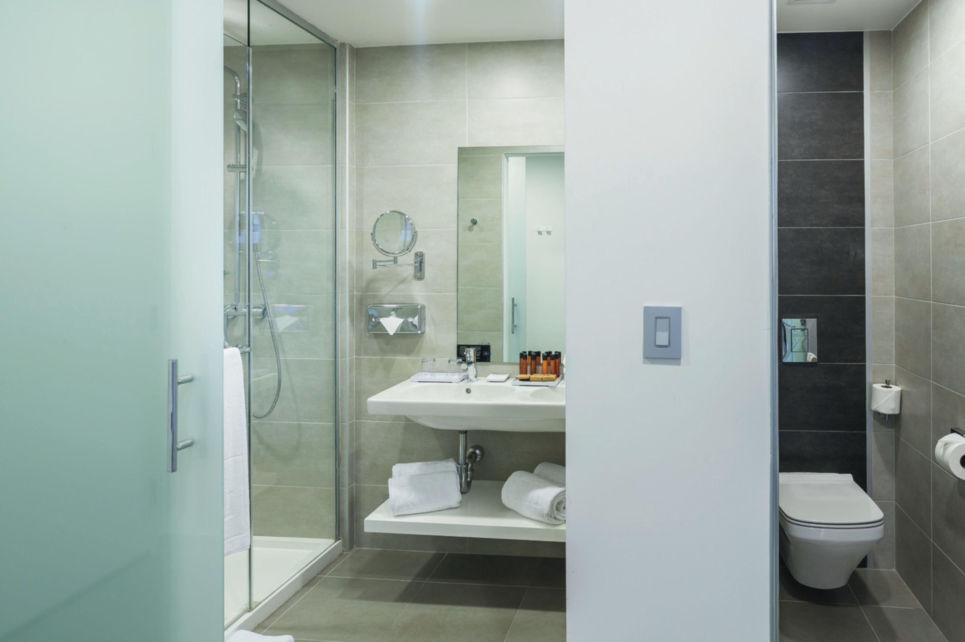 Et moderne badeværelse med brusekabine i glas, vask med spejl og toilet.