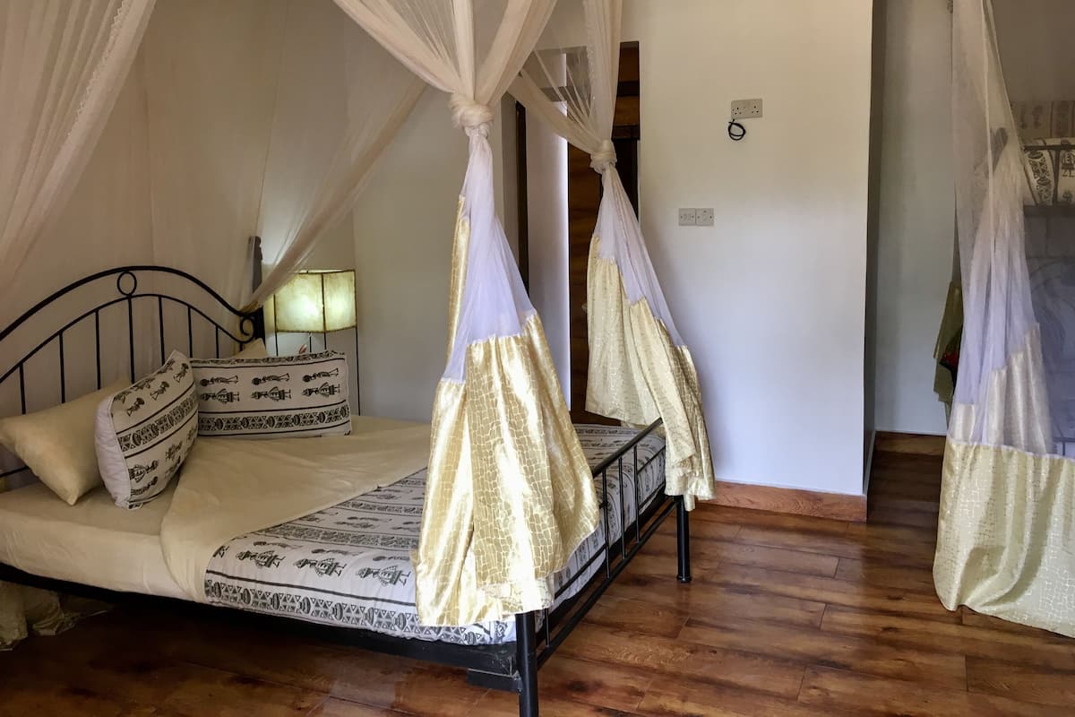 A bedroom with a four-poster canopy bed, patterned bedding, and a nightstand with a lamp.