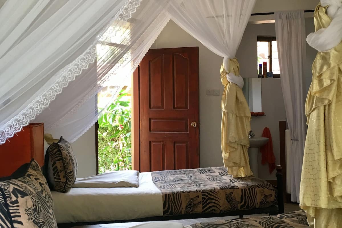 A room with a bed, a window with a view of greenery, a wooden door, and a sink.
