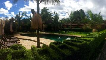 A pool area with stone flooring, palm trees, and neatly trimmed hedges.