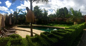 A pool area with stone flooring, palm trees, and neatly trimmed hedges. - Ahadi Lodge (Arusha)