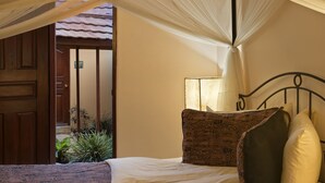 A bedroom with a bed, a canopy, a nightstand, and a door leading to a balcony. - Ahadi Lodge (Arusha)