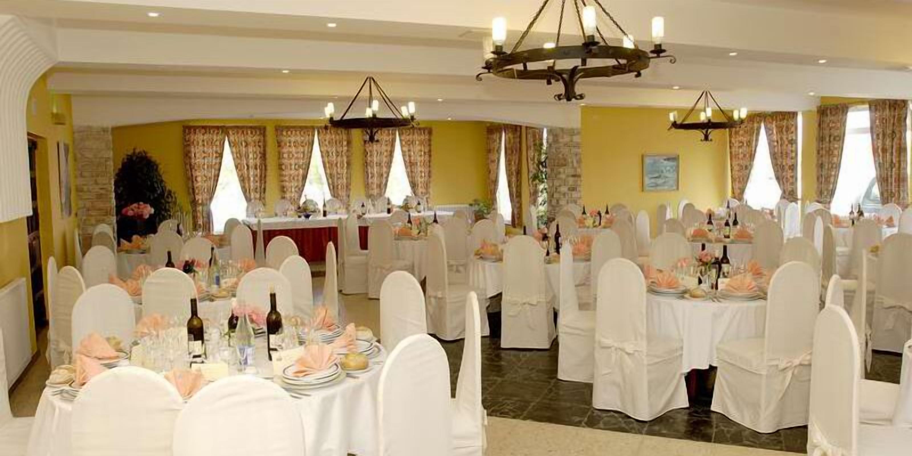 Un salón de banquetes con mesas redondas dispuestas para un evento formal, sillas blancas y candelabros.