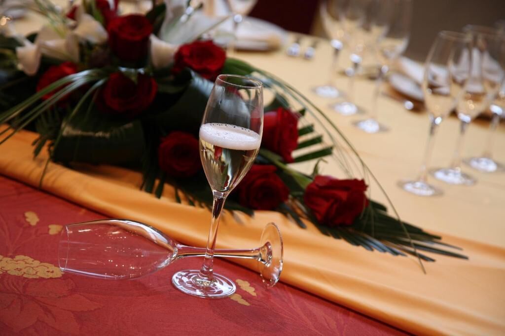 Una mesa dispuesta para un evento formal, con una copa de champán, rosas rojas y un mantel dorado.