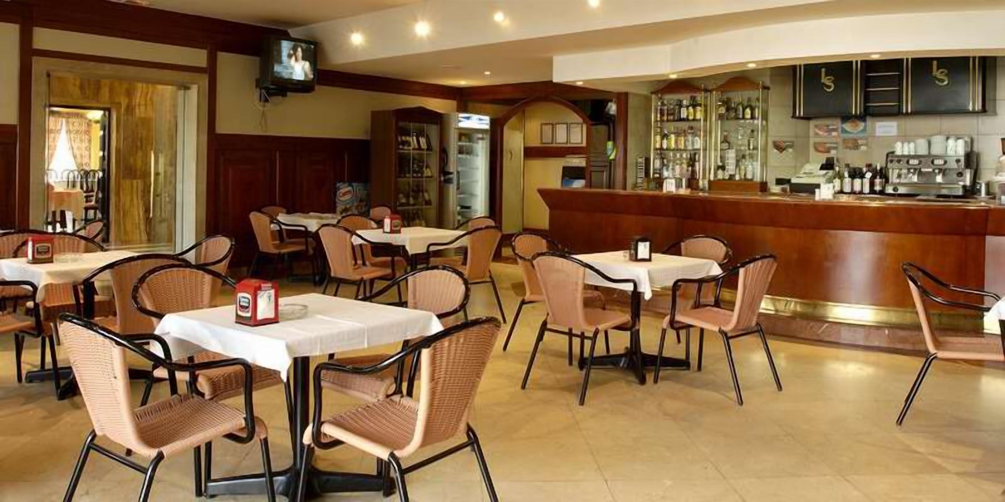 A restaurant with multiple tables and chairs, a bar area with a counter, and a television mounted on the wall.