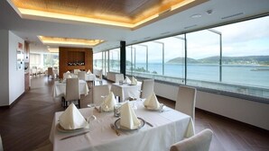 A restaurant with tables set for dining, large windows offering a view of the sea, and a modern ceiling design. - Apartamentos Las Sirenas (Viveiro)