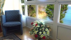 A room with a view of the ocean, a blue armchair, and a floral arrangement. - Apartamentos Las Sirenas (Viveiro)
