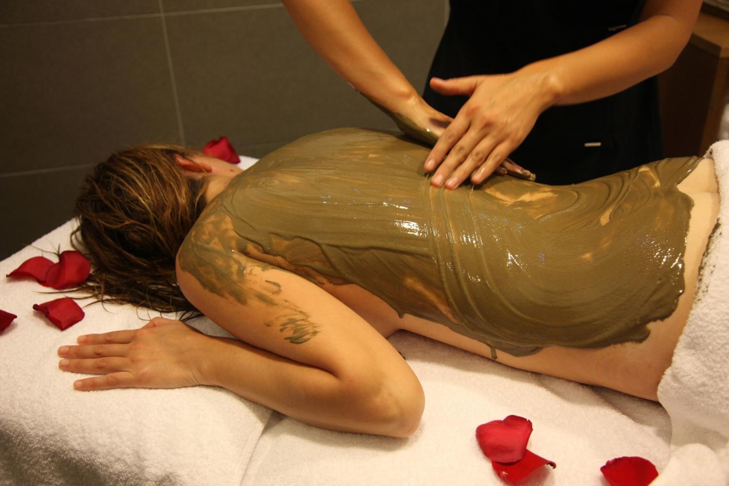 A person receiving a massage with rose petals on the bed.