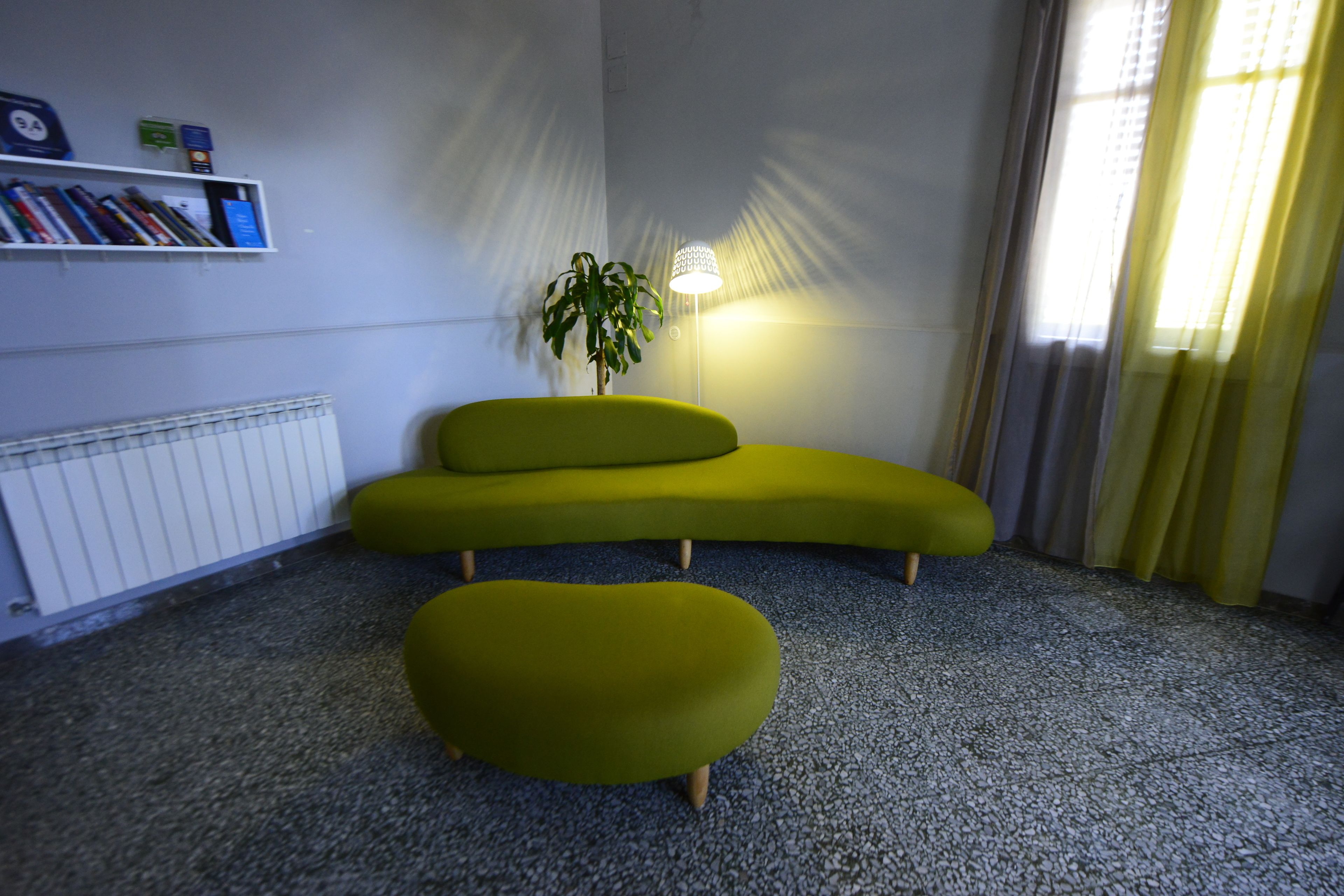 A room with a green sofa, a small table, a potted plant, and a radiator.
