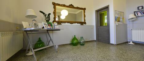 A room with a mirror, a radiator, a desk with a lamp, and two green vases.