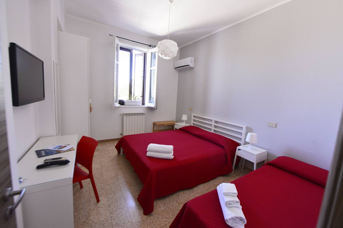 Habitación de hotel con dos camas, un escritorio, una silla, un televisor y una ventana con contraventanas.