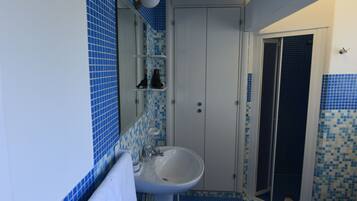 Un baño con lavamanos, espejo y retrete. El suelo y las paredes están cubiertos de azulejos azules.