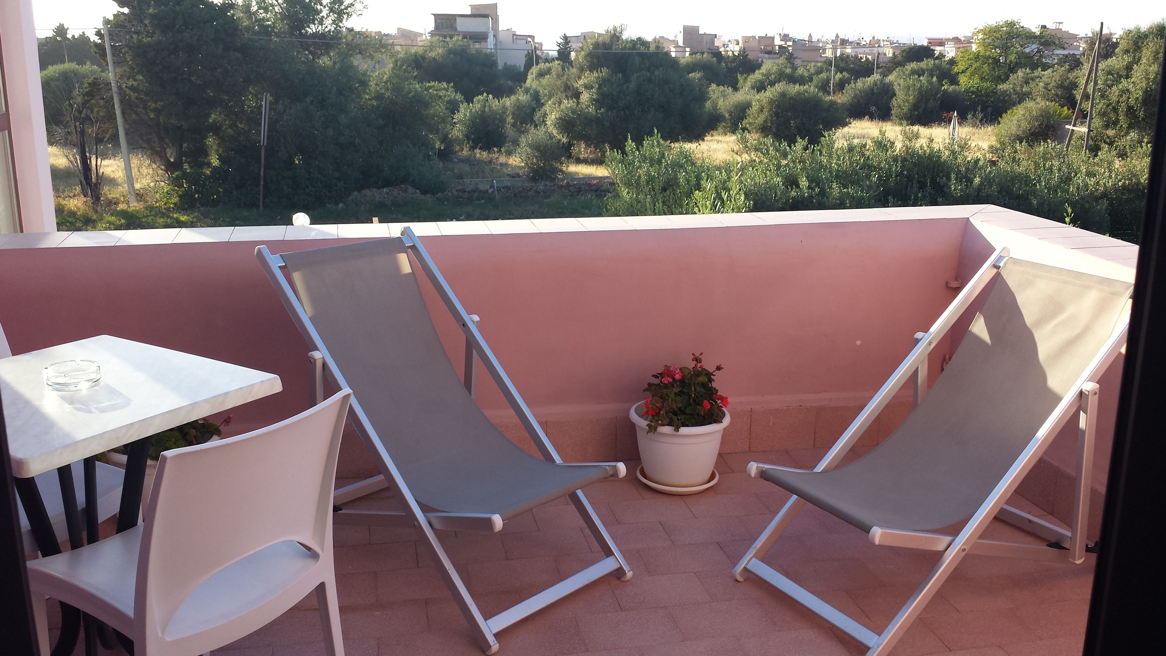 Un balcon avec deux chaises et une table, une plante en pot, et une vue sur un paysage verdoyant avec des bâtiments visibles au loin.