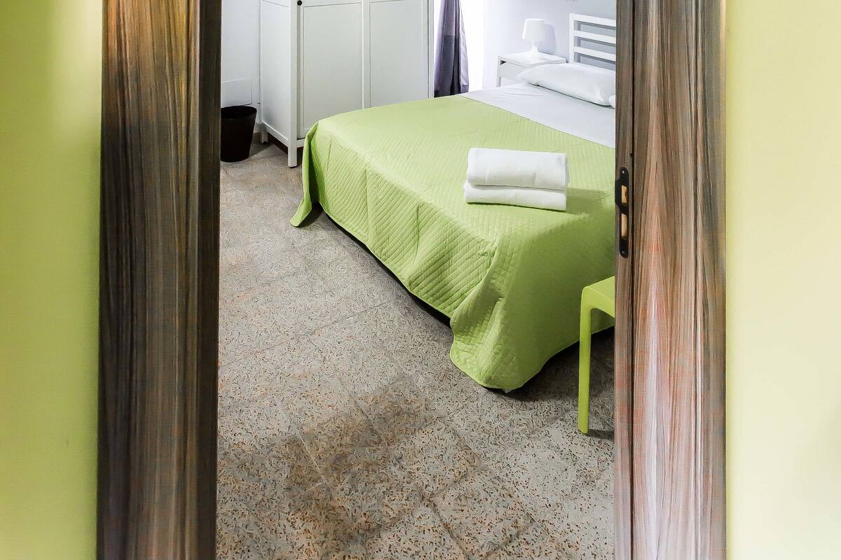 Un dormitorio con colcha verde, armario blanco y techo de madera.