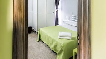 Quarto com colcha verde, guarda-roupa branco e teto de madeira.