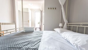 En pænt redt seng med et gråt tæppe og hvide sengetæger, en hvid radiator og en hvid himling.